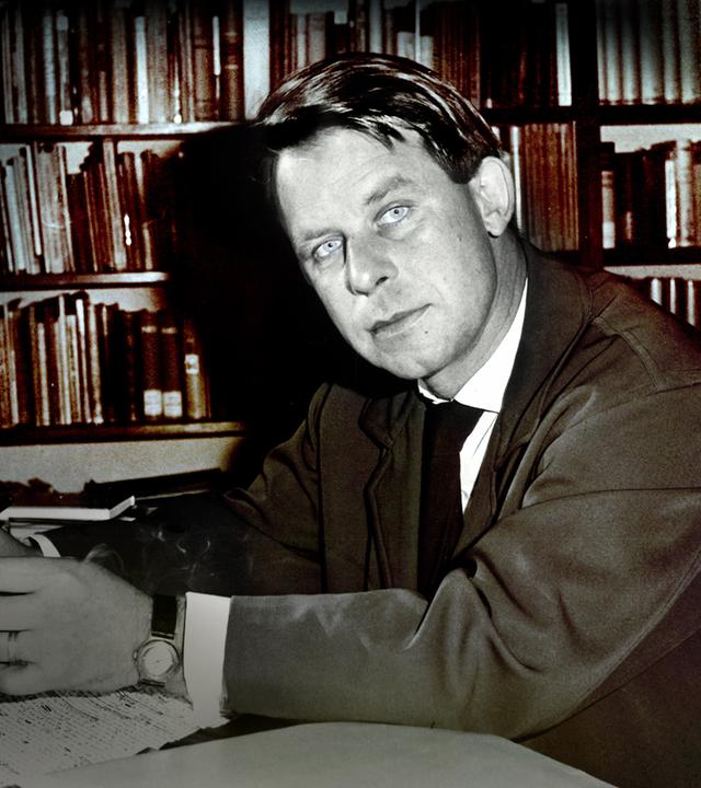  Der junge Siegfried Lenz sitzt vor einer Bücherwand am Schreibtisch (s/w). 