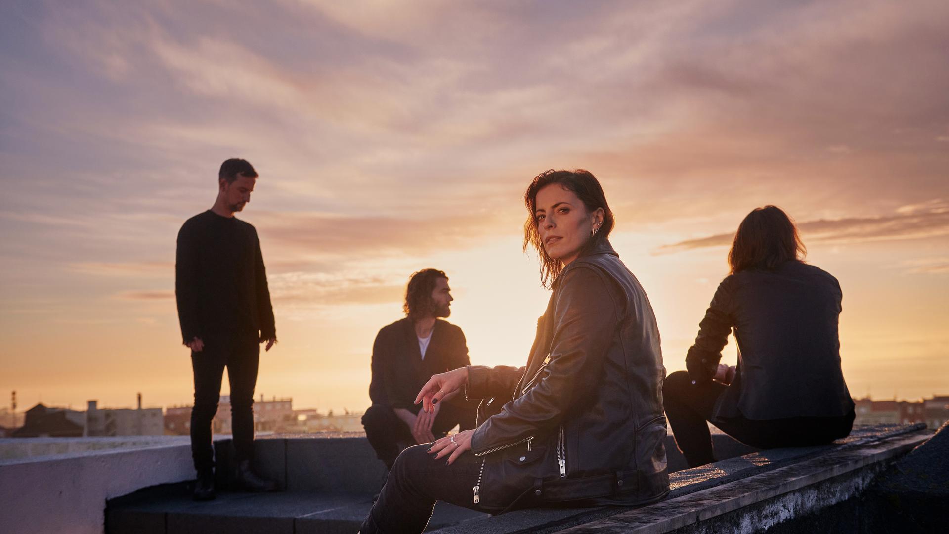 Die vier Bandmitglieder von Silbermond sitzen auf einem Dach, die Sonne geht unter.