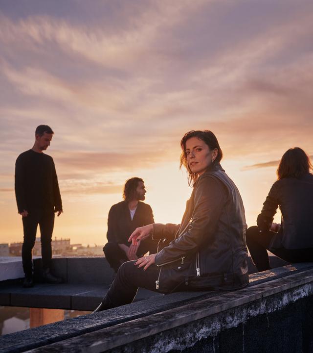 Die vier Bandmitglieder von Silbermond sitzen auf einem Dach, die Sonne geht unter.