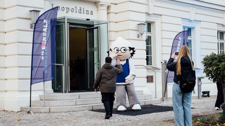 SILBERSALZ Festival 26: Ein Mainzelmännchen-Walker empfängt einen Besucher am Eingang der Leopoldina