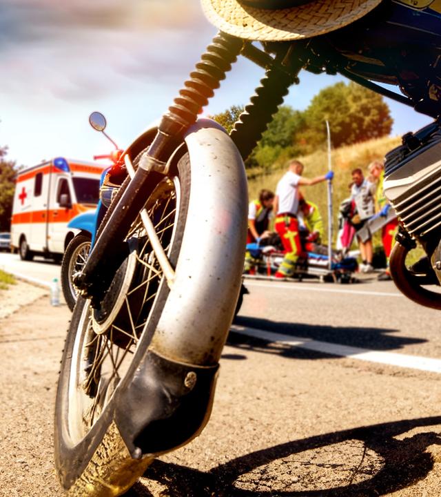Im Vordergrund steht ein blaues Simson-Moped. Im Hintergrund ist eine Unfallszene mit Rettungswagen, Sanitätern und einem Menschen, der auf einer Trage liegt, zu sehen. Die Perspektive auf die Szenerie ist KI-generiert.