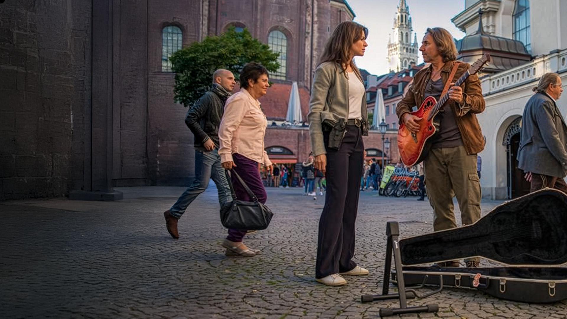 "SOKO München - Sinfonie der Großstadt": Katharina Hahn (Bianca Hein) steht mit Edgar Seiler (Dieter Landuris) in der Münchner Innenstadt und unterhält sich mit ihm. Die beiden sehen sich ernst an. Edgar Seiler hat seine Gitarre umhängen und spielt darauf. Neben ihm steht ein geöffneter Gitarrenkasten und ein Gitarrenständer. Hinter Katharina Hahn und Edgar Seiler laufen zwei Frauen und zwei Männer vorbei. Im Hintergrund sieht man weitere Menschen in der Innenstadt stehen.