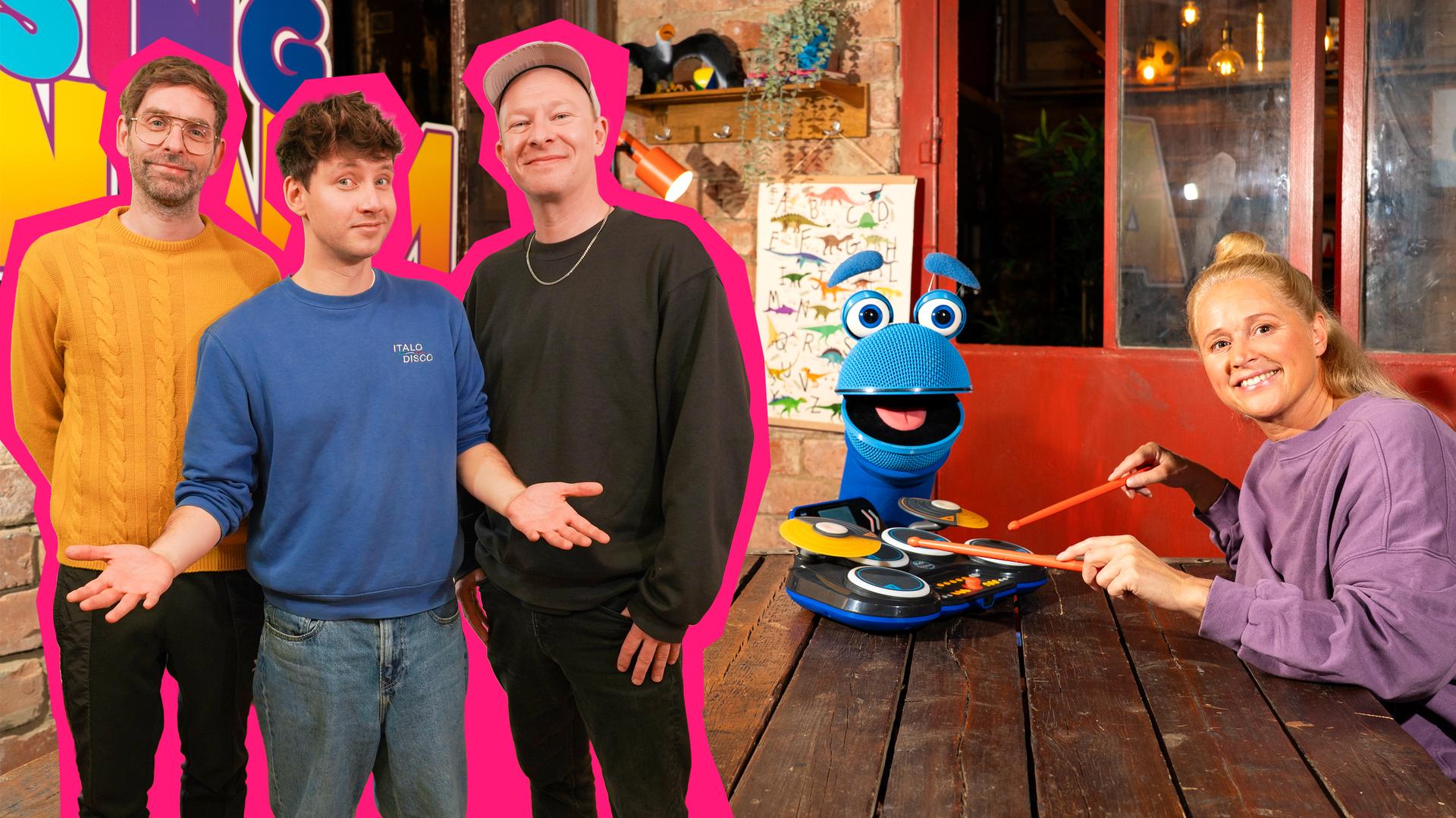 Singa (l.) und SingDing (r.) sitzen am Küchentisch. Vor Singa steht ein Spielzeug-Schlagzeug. Die Band "Deine Freunde" steht link im Bild.