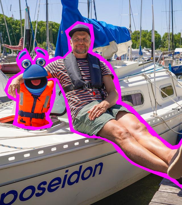 "Singalarm - SingDing auf hoher See": Herr Jan und SingDing sitzen auf einem weißen Segelboot, das an einem Holzsteg in einem Yachthafen angelegt hat. SingDing trägt eine orangefarbene Rettungsweste, Herr Jan hat den Arm um SingDing gelegt und die Beine ausgestreckt.