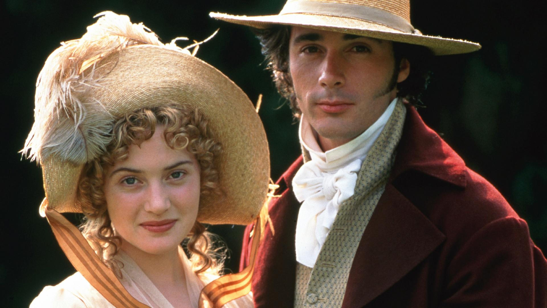 Kate Winslet und Huge Grant in historischem Kostüm halten sich die Hände und schauen in die Kamera.