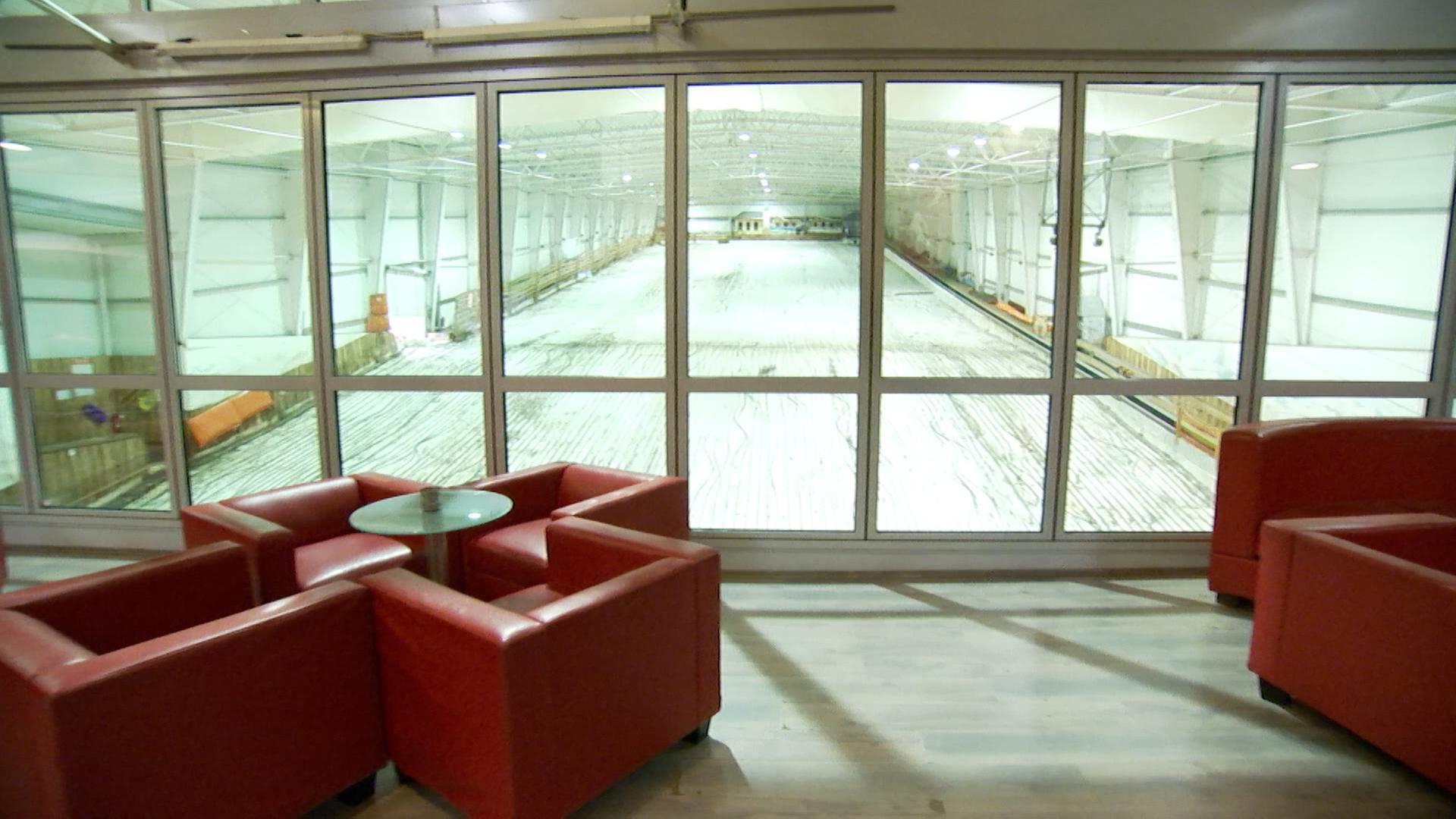 In der Skihalle in Brandeburg stehen rote Sessel in einem Raum, von welchem man auf die Piste hinunter schauen kann. 