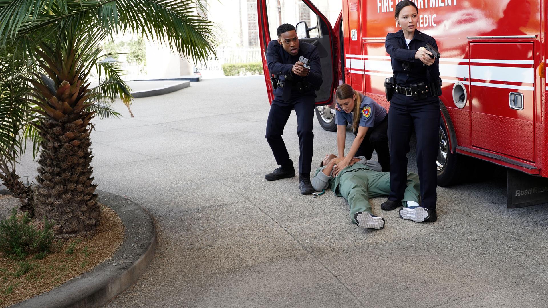 "The Rookie - Skrupellos": Jackson West (Titus Makin Jr.) und Lucy Chen (Melissa O'Neil) zielen mit ihren Waffen zur Seite. Auf dem Boden liegt ein verletzter Mann. Eine weitere Beamtin (Komparsin) gibt ihm eine Herzdruckmassage.