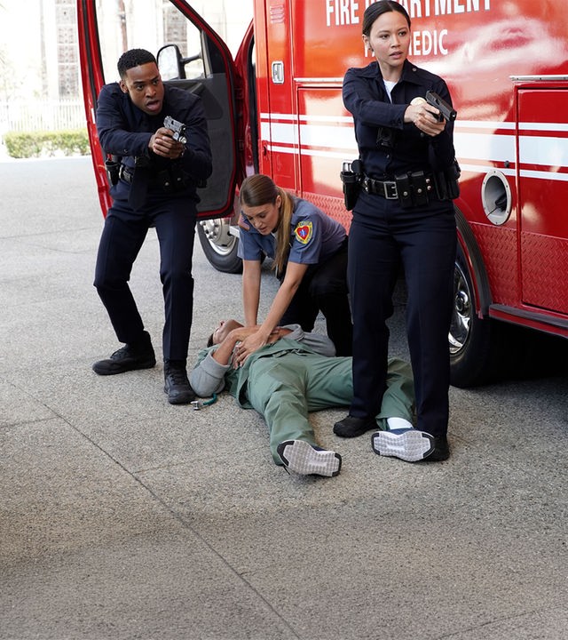 "The Rookie - Skrupellos": Jackson West (Titus Makin Jr.) und Lucy Chen (Melissa O'Neil) zielen mit ihren Waffen zur Seite. Auf dem Boden liegt ein verletzter Mann. Eine weitere Beamtin (Komparsin) gibt ihm eine Herzdruckmassage.