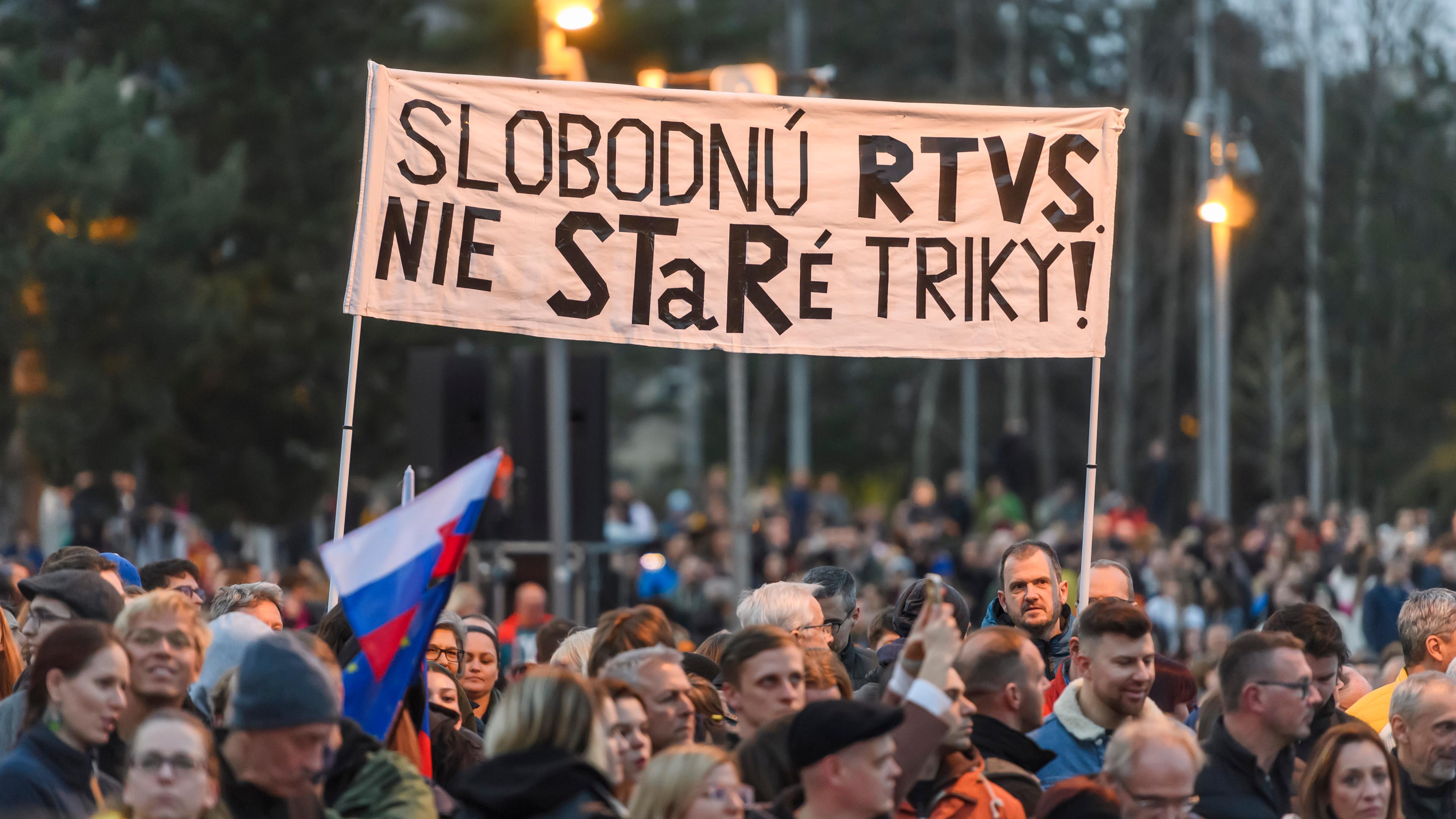 Eine Menschenmenge steht mit Schildern und Fahnen auf einem großen Platz. Auf den Schildern stehen slowakische Sprüche, es wehen slowakische Fahnen.