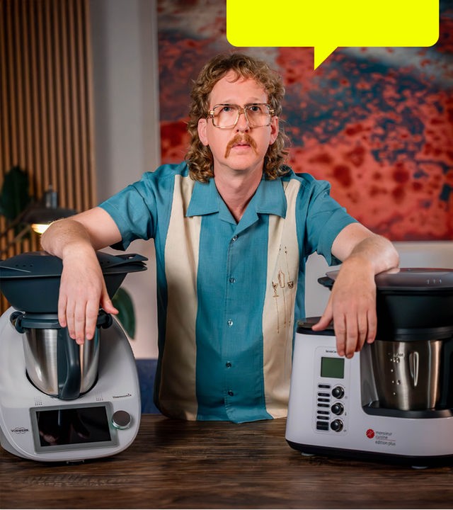 Uke Bosse schaut ernst in die Kamera, seine Arme stützen sich links auf einen Thermomix und rechts auf eine "Monsieur Cuisine"-Maschine.