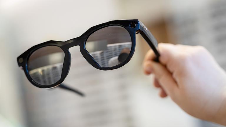  Eine Frau hält in einem Brillenfachgeschäft eine smarte Datenbrille der Firma Oakley Meta in ihrer Hand.