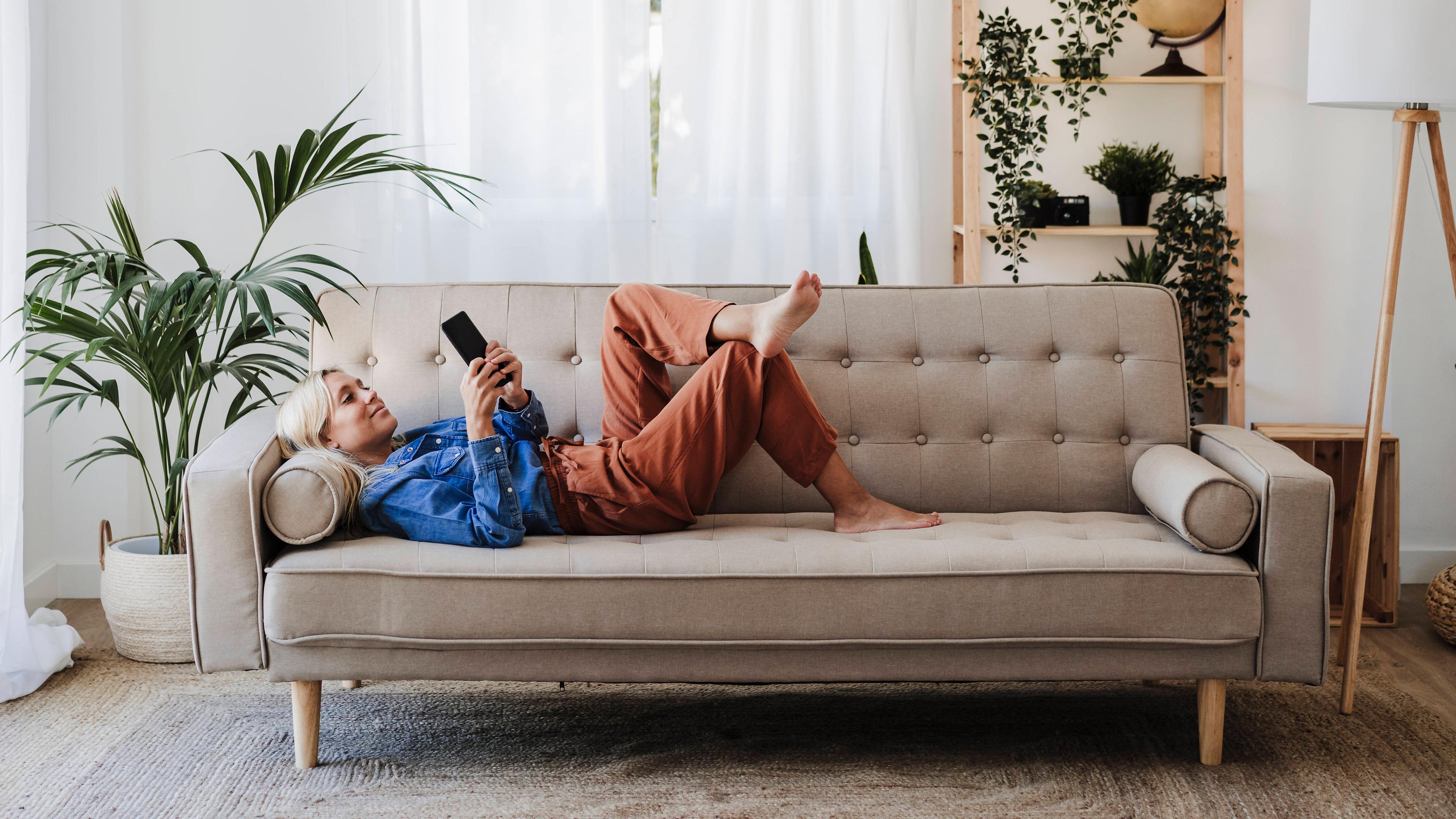 Eine Frau liegt auf auf der Couch und hält ihr Smartphone in der Hand, aufgenommen am 09.08.2022