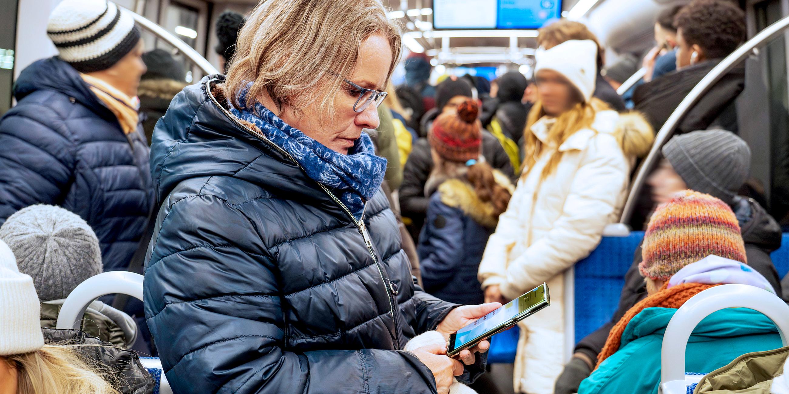 Frau liest Nachrichten auf ihrem Smartphone, in der vollbesetzten U-Bahn