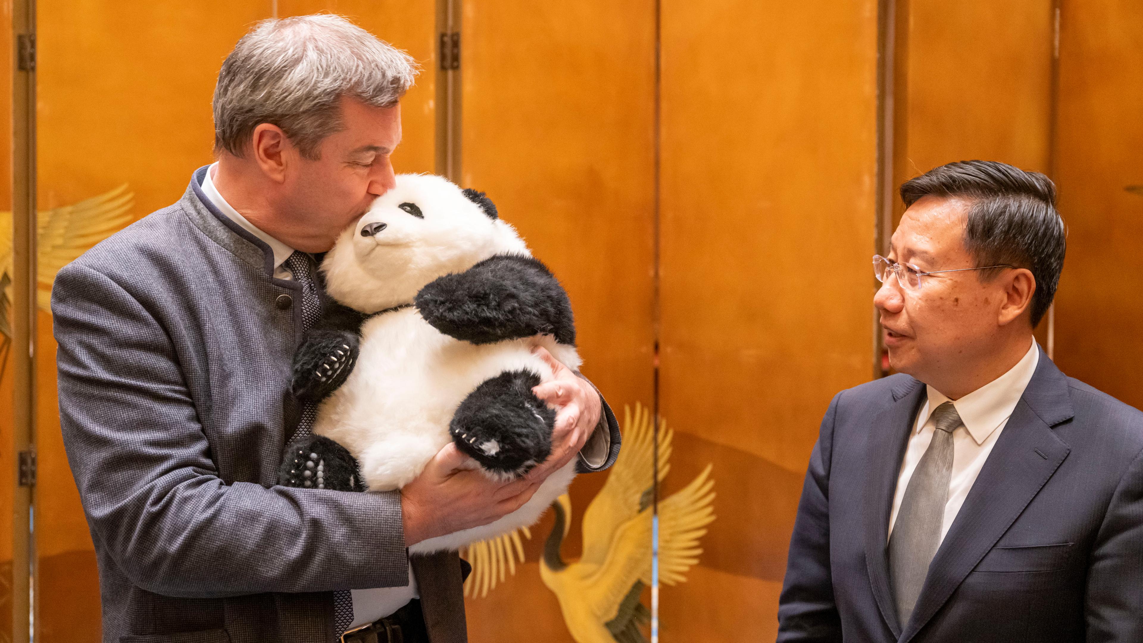 Der bayrische Ministerpräsident Markus Söder, hält einen Pandabären aus Plüsch in den Armen, den er zuvor von Wang Xiaohui, Parteisekretär der Kommunistischen Partei, als Gastgeschenk überreicht bekommen hat.