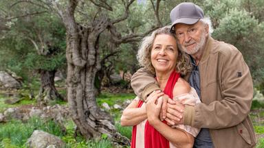 Das Ehepaar Renate (Michaela May) und Kurt (Michael Gwisdek) Lehmann steht in einer Umarmung in einem Olivenhain und lächelt glücklich.