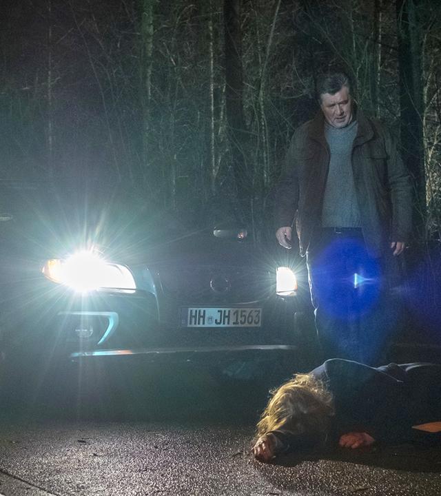 "Notruf Hafenkante - SOKO Kiebitz": Hans Moor (Bruno F. Apitz) steht im Dunkeln auf einer Landstraße vor seinem Auto und schaut entsetzt auf eine Frau (Tanja Schleiff), die auf der Straße vor ihm liegt. Im Hintergrund ist Wald zu sehen.