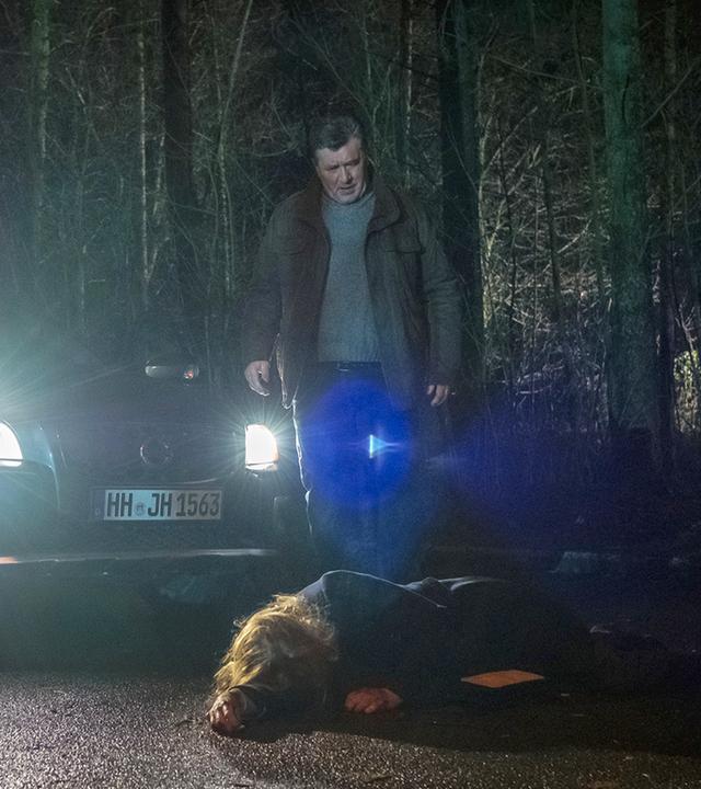 "Notruf Hafenkante - SOKO Kiebitz": Hans Moor (Bruno F. Apitz) steht im Dunkeln auf einer Landstraße vor seinem Auto und schaut entsetzt auf eine Frau (Tanja Schleiff), die auf der Straße vor ihm liegt. Im Hintergrund ist Wald zu sehen.