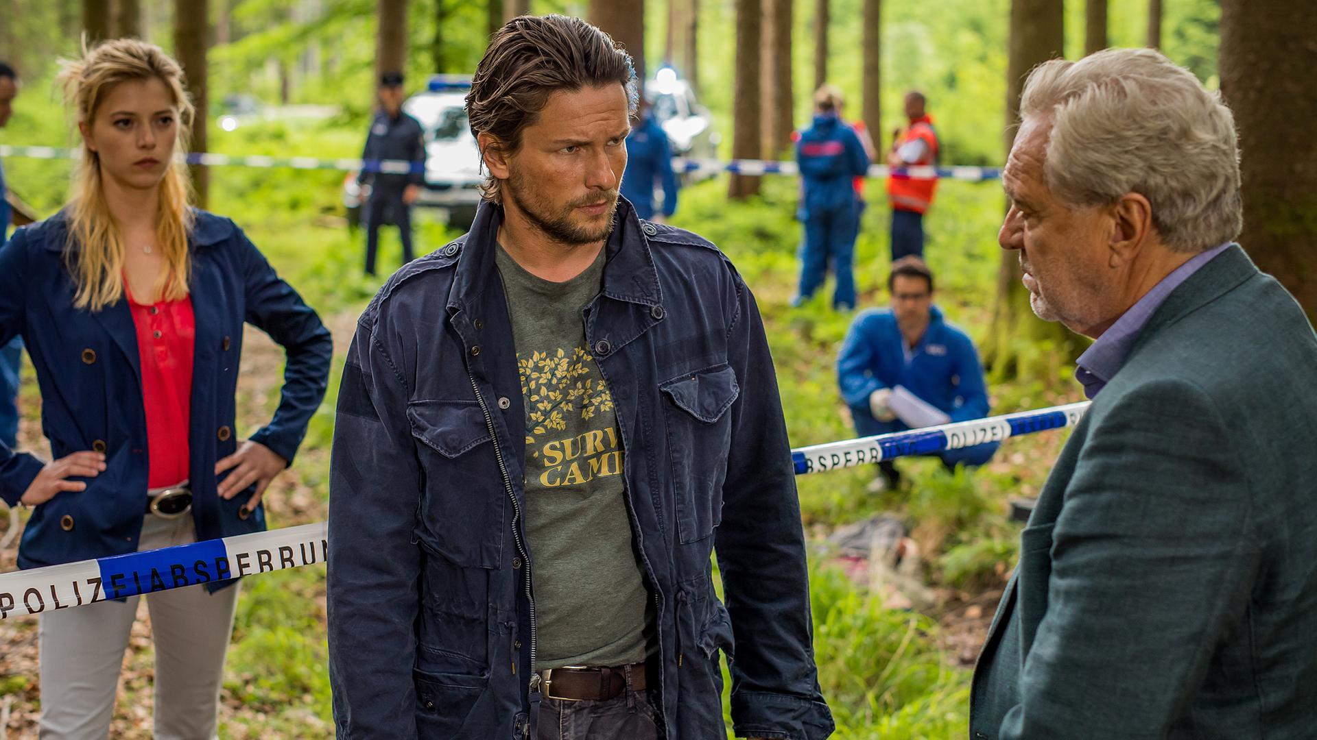 Arthur Bauer (Gerd Silberbauer) und Resi Schwaiger (Mersiha Husagic) befinden sich im Wald an einem Tatort. Zwischen ihnen steht Uwe Zöllner (Bert Tischendorf), der sich mit Arthur Bauer unterhält.