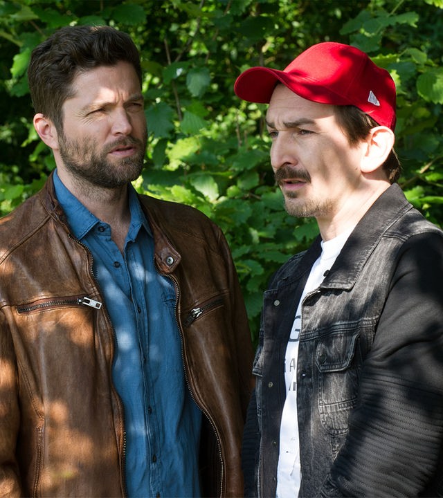 "SOKO Stuttgart - Cool bleiben": Jo Stoll (Peter Ketnath) und Bertram Fuchs (Till Wonka) sprechen miteinander. Sie stehen vor einem Gebüsch und sehen in unterschiedliche Richtungen.
