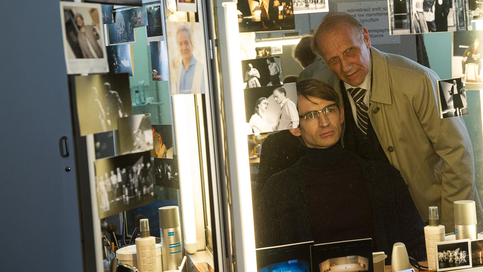 "SOKO Stuttgart - Letzter Vorhang": Daan Wachtel (Arne Fiedler) sitzt vor einem Maskenspiegel voller Fotos der Schauspieler. Hinter ihm steht Michael Kaiser (Karl Kranzkowski) und beäugt ihn genau.