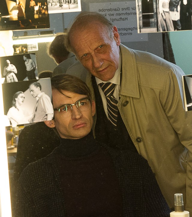 "SOKO Stuttgart - Letzter Vorhang": Daan Wachtel (Arne Fiedler) sitzt vor einem Maskenspiegel voller Fotos der Schauspieler. Hinter ihm steht Michael Kaiser (Karl Kranzkowski) und beäugt ihn genau.