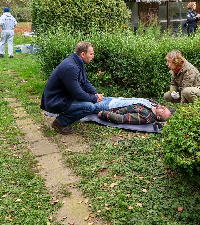 "SOKO Wismar – Der Heimkehrer": Dr. Helene Sturbeck (Katharina Blaschke) und Lars Pöhlmann (Dominic Boeer) knien vor Sven Thalers Leiche (Matijas Versic). Im Hintergrund befragt Paula Moorkampf (Stella Hinrichs) den Makler Hansen (Leif Evers), der den Toten entdeckt hat.