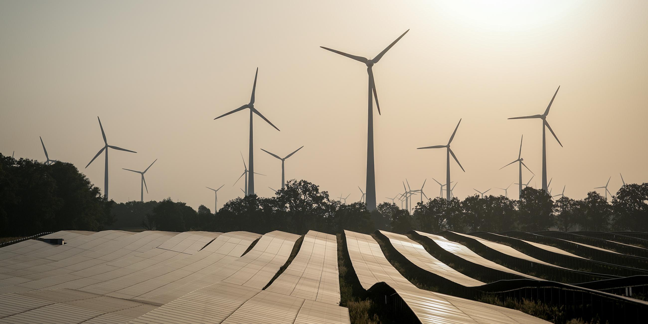 Ein Solarfeld reflektiert vor Windkraftanlagen die Sonnenstrahlen. 