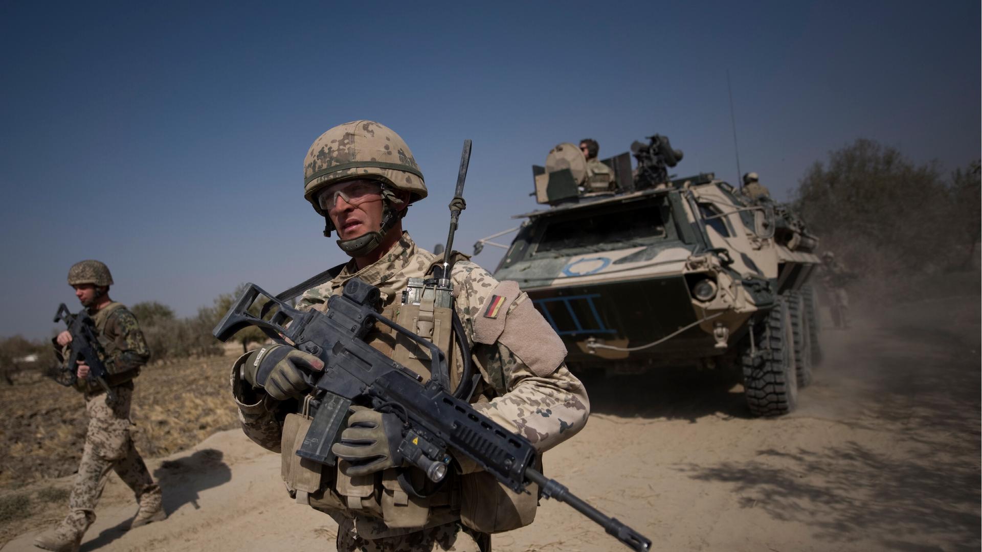 Soldaten gehen vor einem Panzer auf einer staubigen Stra&szlig;e