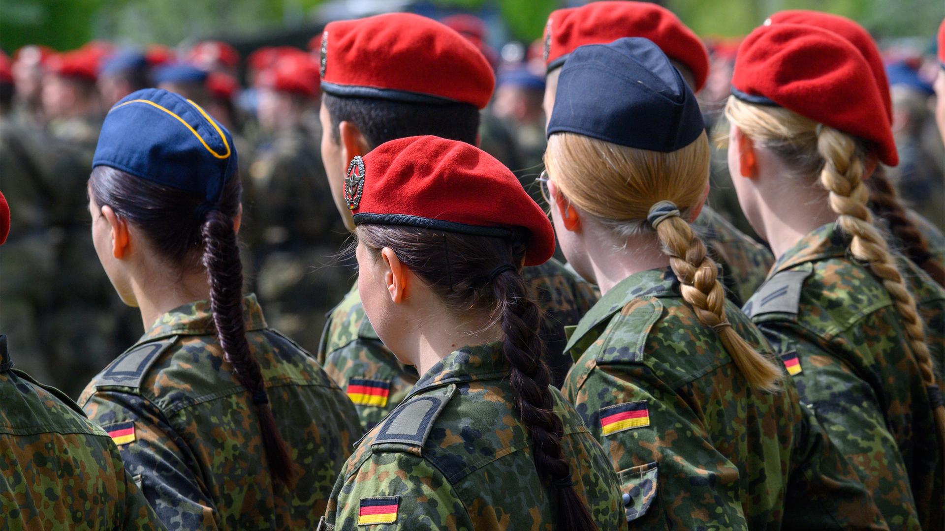 Rückansicht von weiblichen und männlichen Rekruten der Bundeswehr, die zum Gelöbnis stramm stehen.