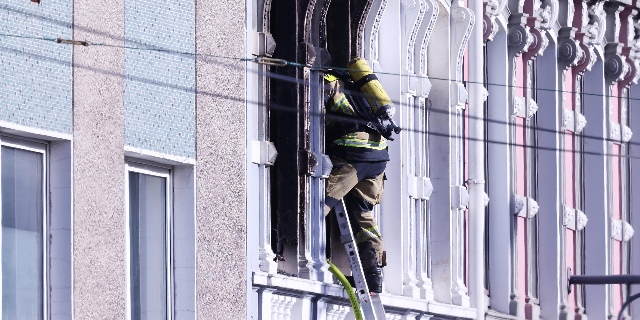 Ein Feuerwehrmann klettert an einem Haus, in dem es gebrannt hat, auf einer Leiter. 