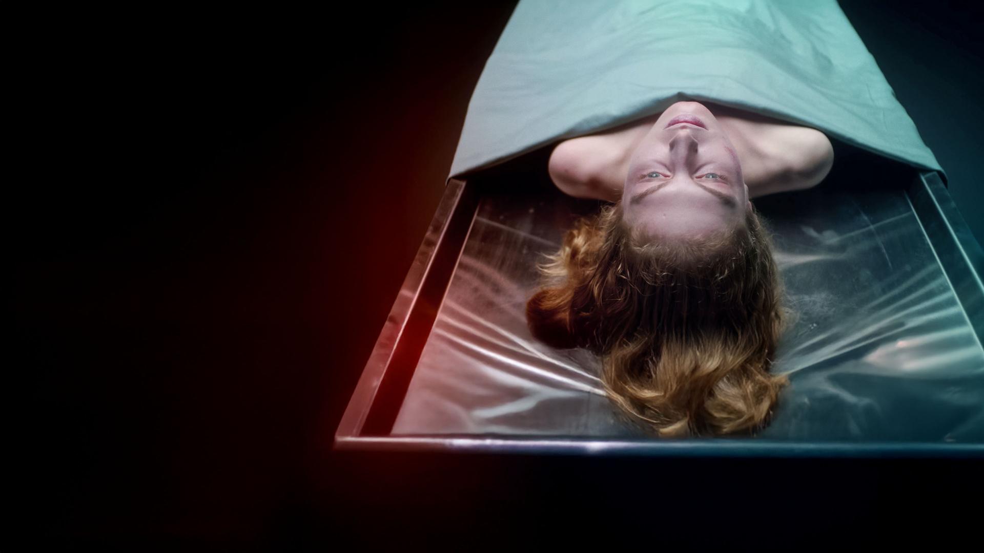 Die Leiche einer Frau liegt auf einem Obduktionstisch. Ihr Kopf und die Schulterpartie ragen unter einem Tuch hervor.