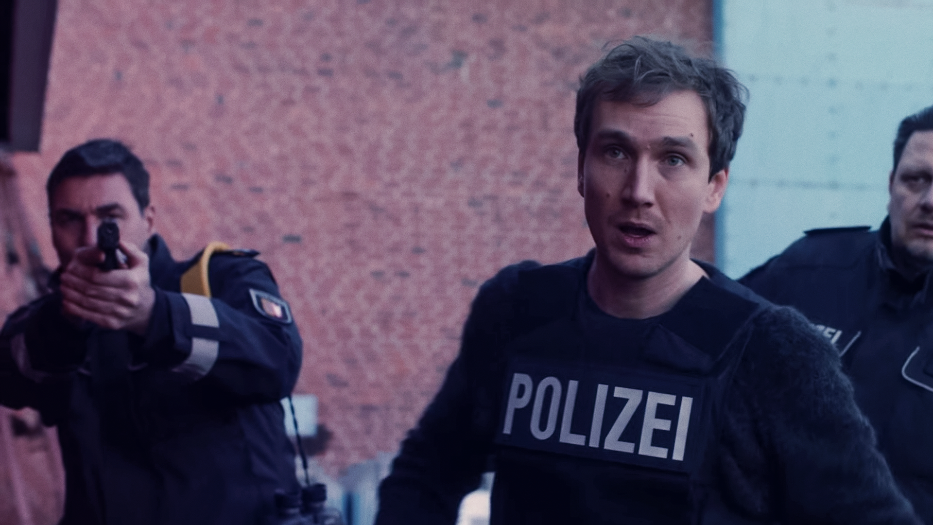 Simon (Jan Krauter) im Einsatz mit schusssicherer Polizeiweste. Hinter ihm zwei Kollegen.
