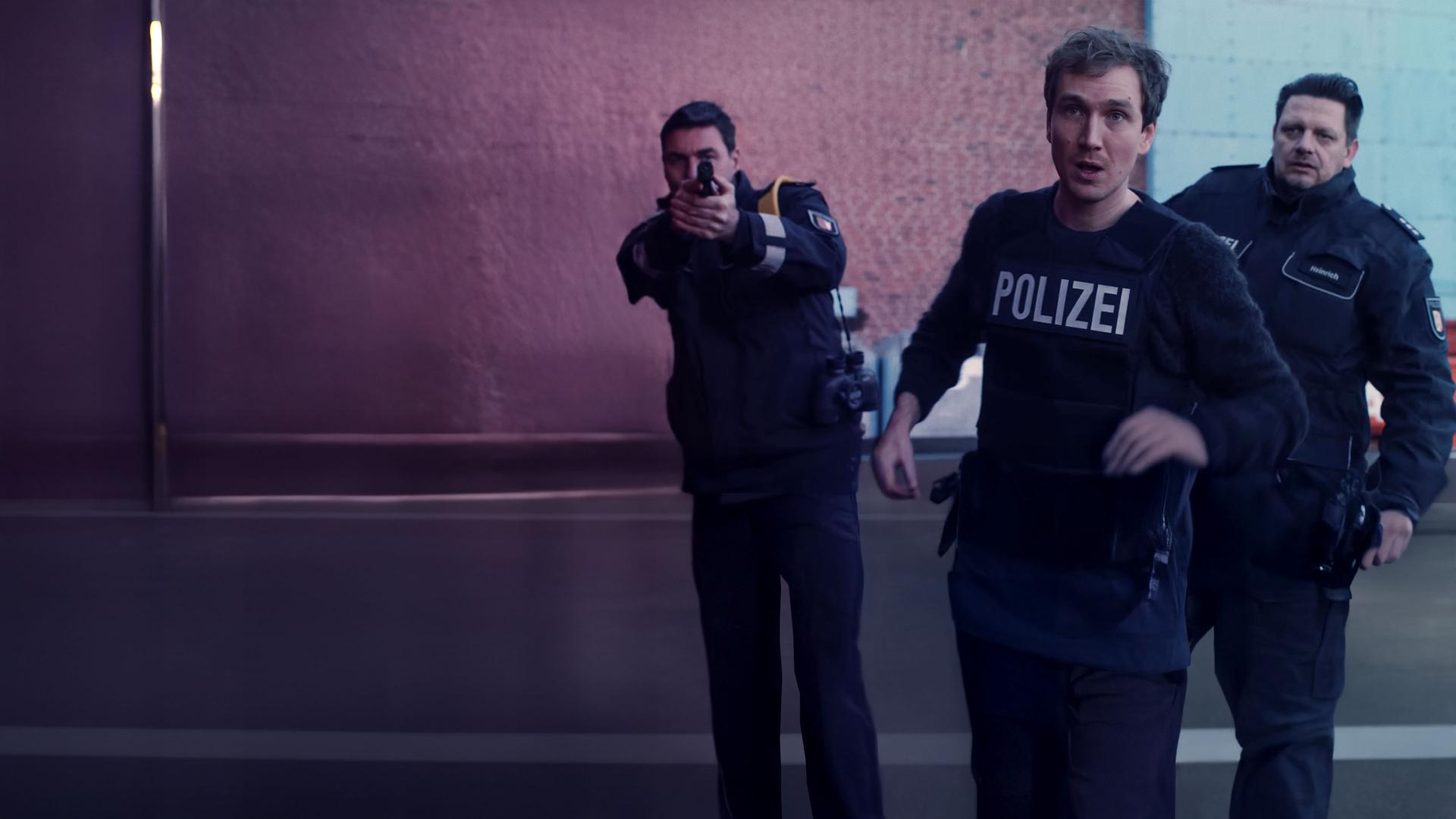 Simon (Jan Krauter) im Einsatz mit schusssicherer Polizeiweste. Hinter ihm zwei Kollegen.