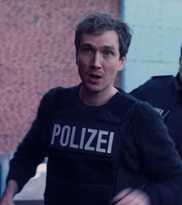 Simon (Jan Krauter) im Einsatz mit schusssicherer Polizeiweste. Hinter ihm zwei Kollegen.