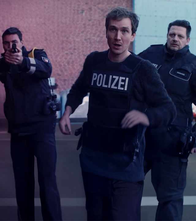Simon (Jan Krauter) im Einsatz mit schusssicherer Polizeiweste. Hinter ihm zwei Kollegen.