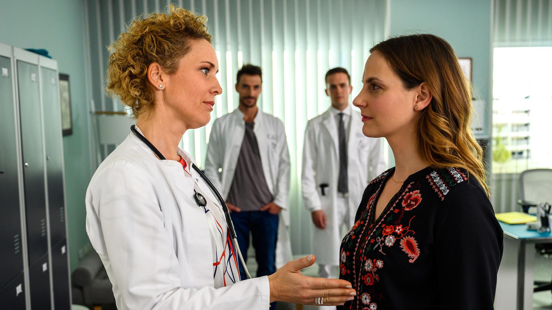 Hanna Winter (Marie Zielcke) verabschiedet sich von Dr. Helena von Arnstett (Claudia Hiersche). Dr. Frank Stern (Max Alberti) und Dr. Tobias Lewandowski (Eric Klotzsch) stehen im Hintergrund und beobachten die beiden.