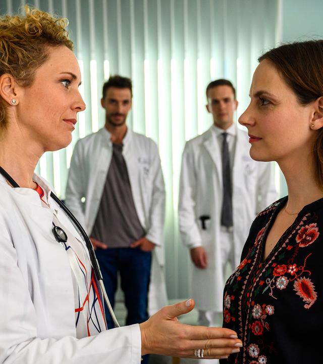 Hanna Winter (Marie Zielcke) verabschiedet sich von Dr. Helena von Arnstett (Claudia Hiersche). Dr. Frank Stern (Max Alberti) und Dr. Tobias Lewandowski (Eric Klotzsch) stehen im Hintergrund und beobachten die beiden.