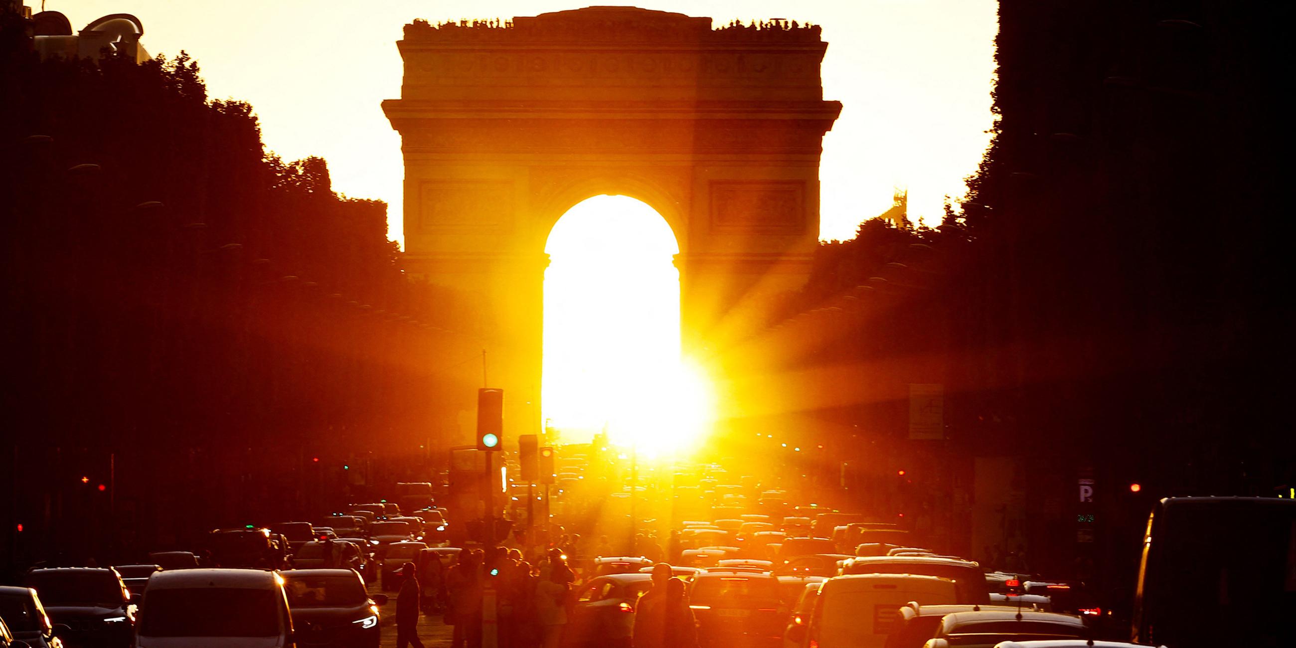 Autos fahren vor dem Arc de Triomphe während die Sonne untergeht.