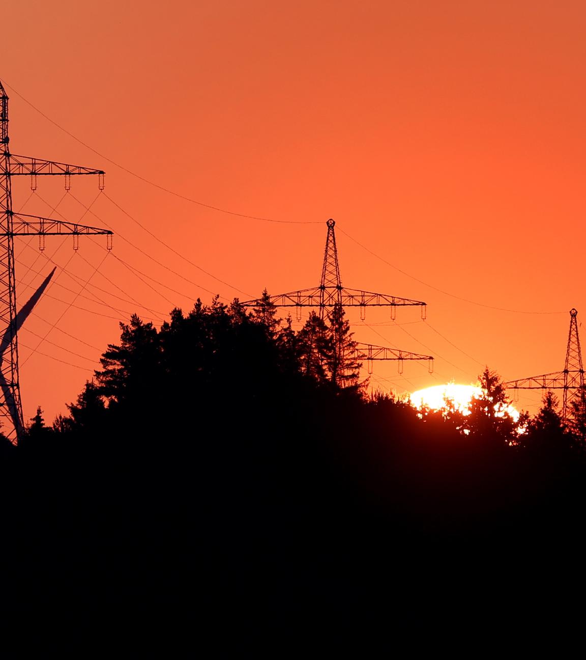 Die Sonne geht hinter einem Windrad und Strommasten auf, der Himmel ist orange-rot. 
