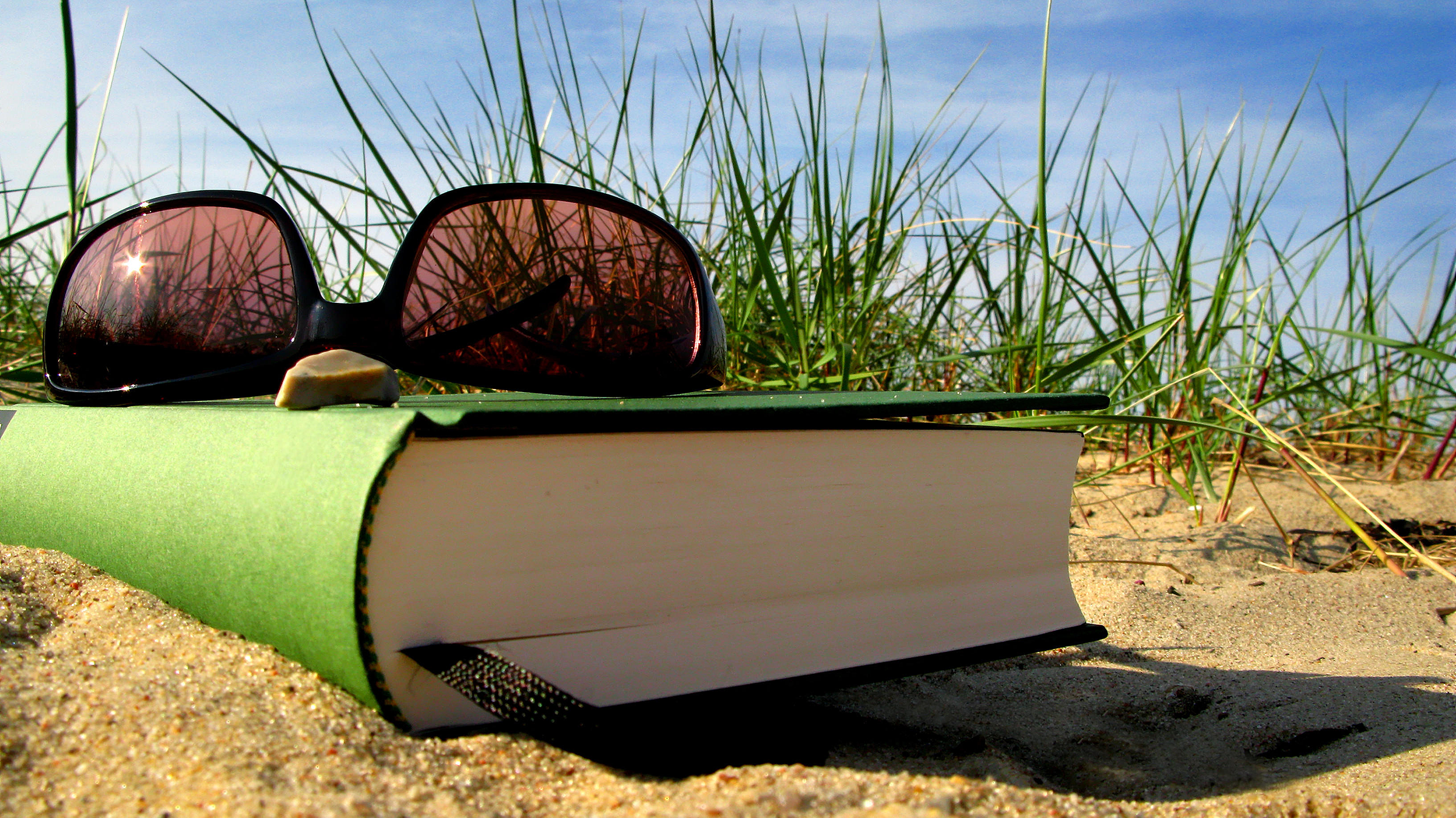 Buch und Sonnenbrille liegen am Strand