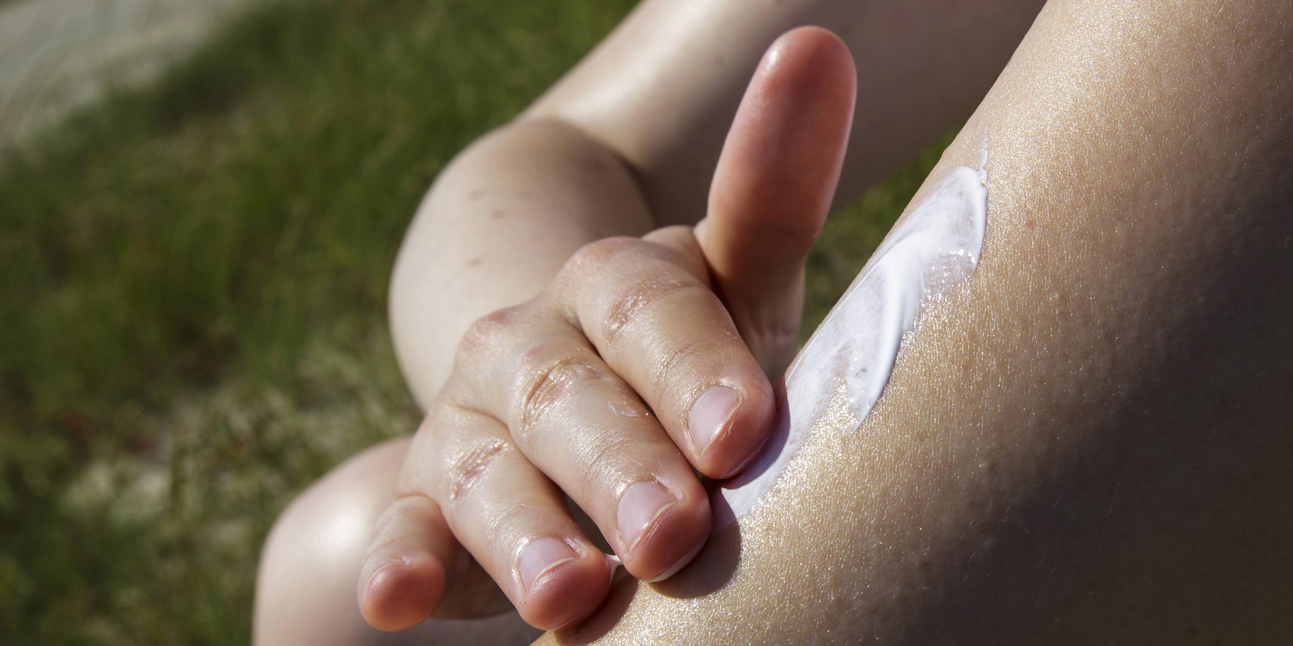 Eine Frau reibt sich den Arm mit Sonnencreme ein. 