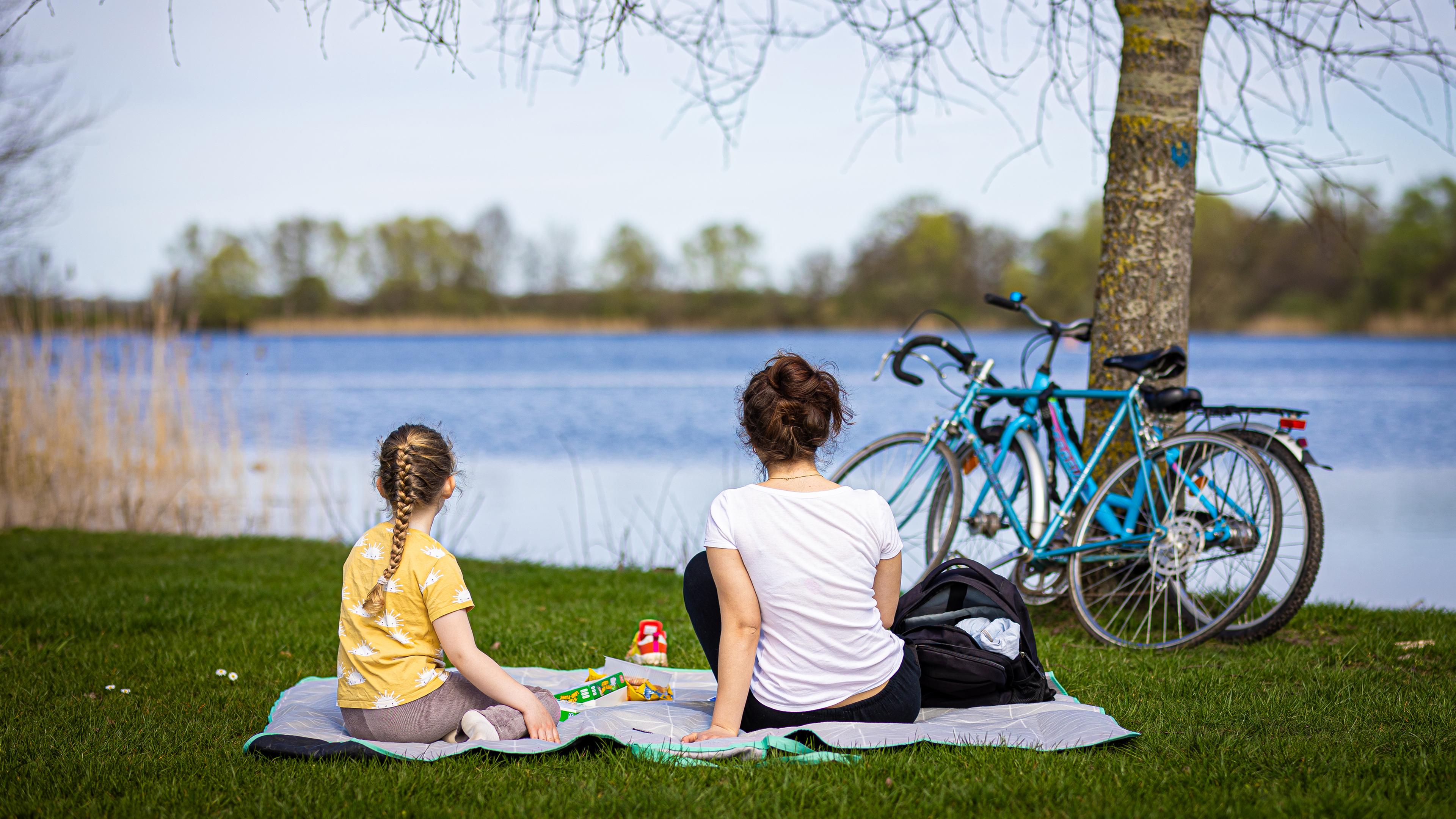 Niedersachsen, Isernhagen: Eine Frau und ein Kind sitzen bei sonnigem Wetter am Ufer vom Hufeisensee in der Region Hannover.