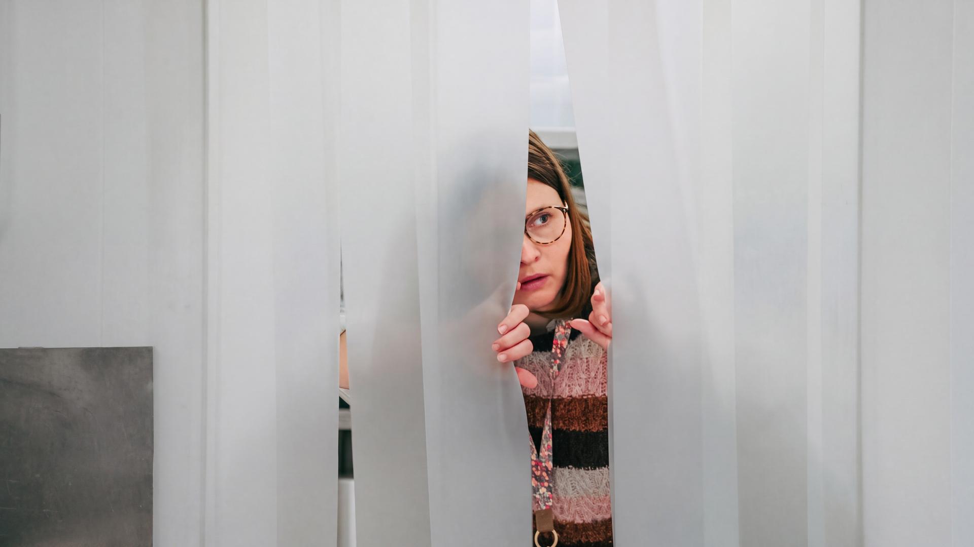"Nine to Five - Das Amt - Sonntag Nichts vor": Conny (Lisa Hrdina) blickt durch einen Lamellenvorhang.