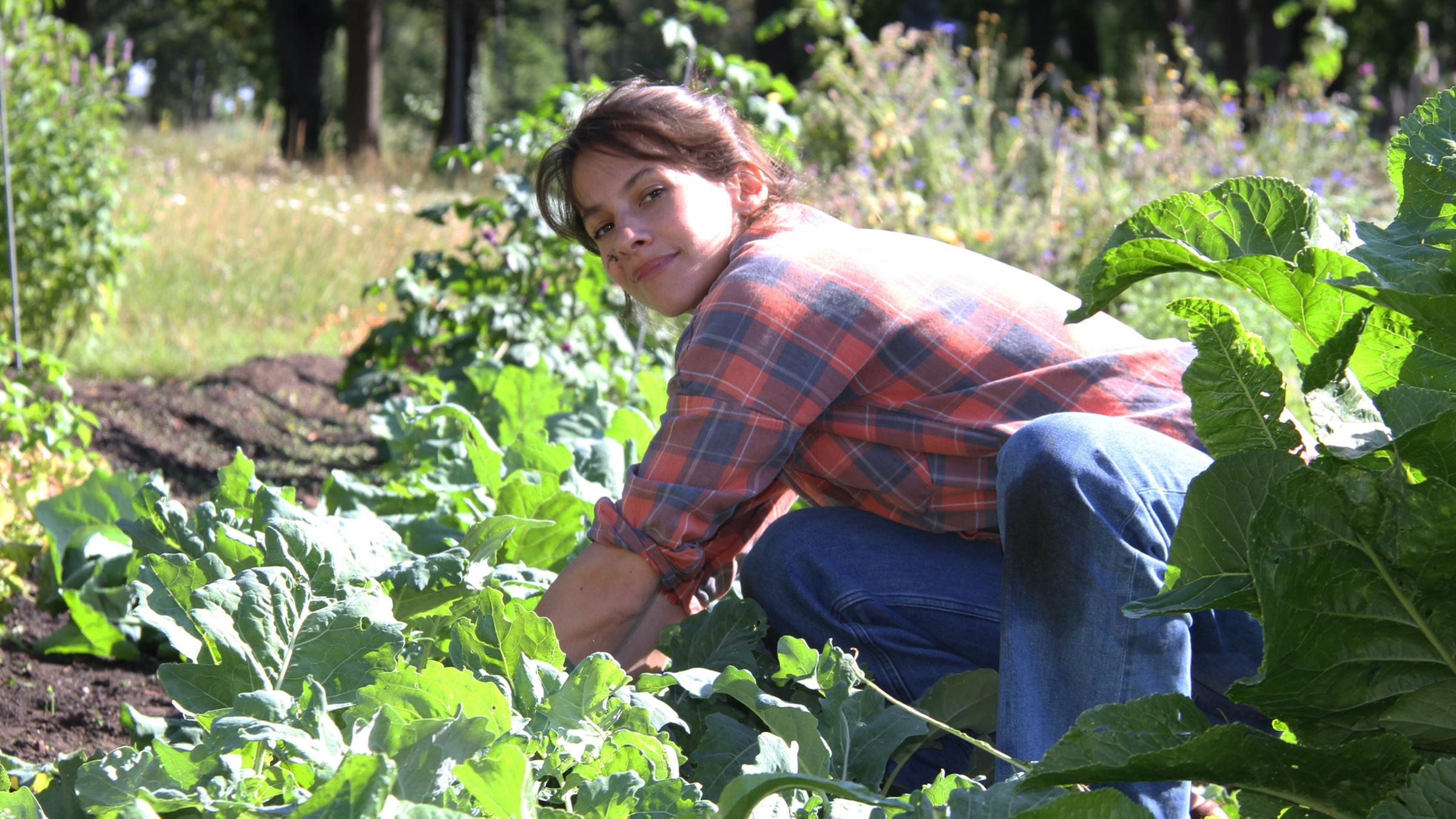Maria Giménez erntet Kohlrabi und schaut dabei lächelnd in die Kamera.