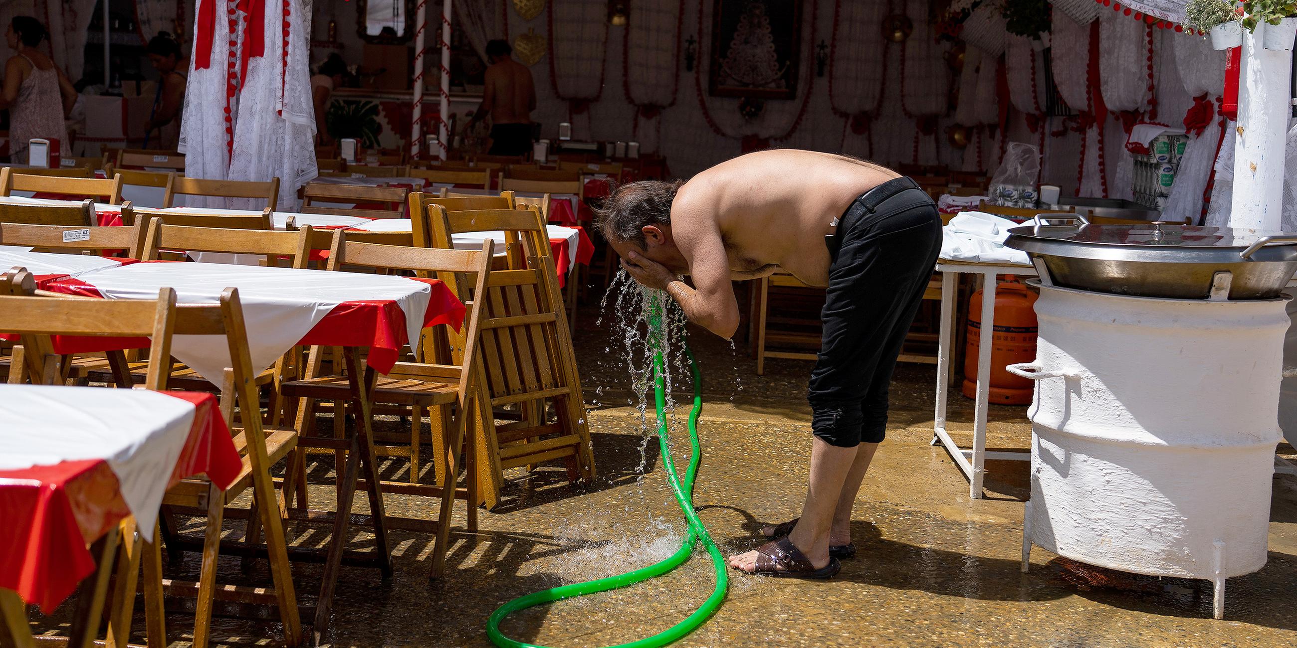 Ein Mann erfrischt sich an einem Wasserschlauch in Sevilla, Spanien