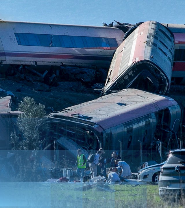 Verunglückte Wagons nach der Kollision zwei spanischer Züge, Teile eines Wagons hängen einen Hang hinunter und sind zerstört, Rettungskräfte sind an der Unfallstelle.