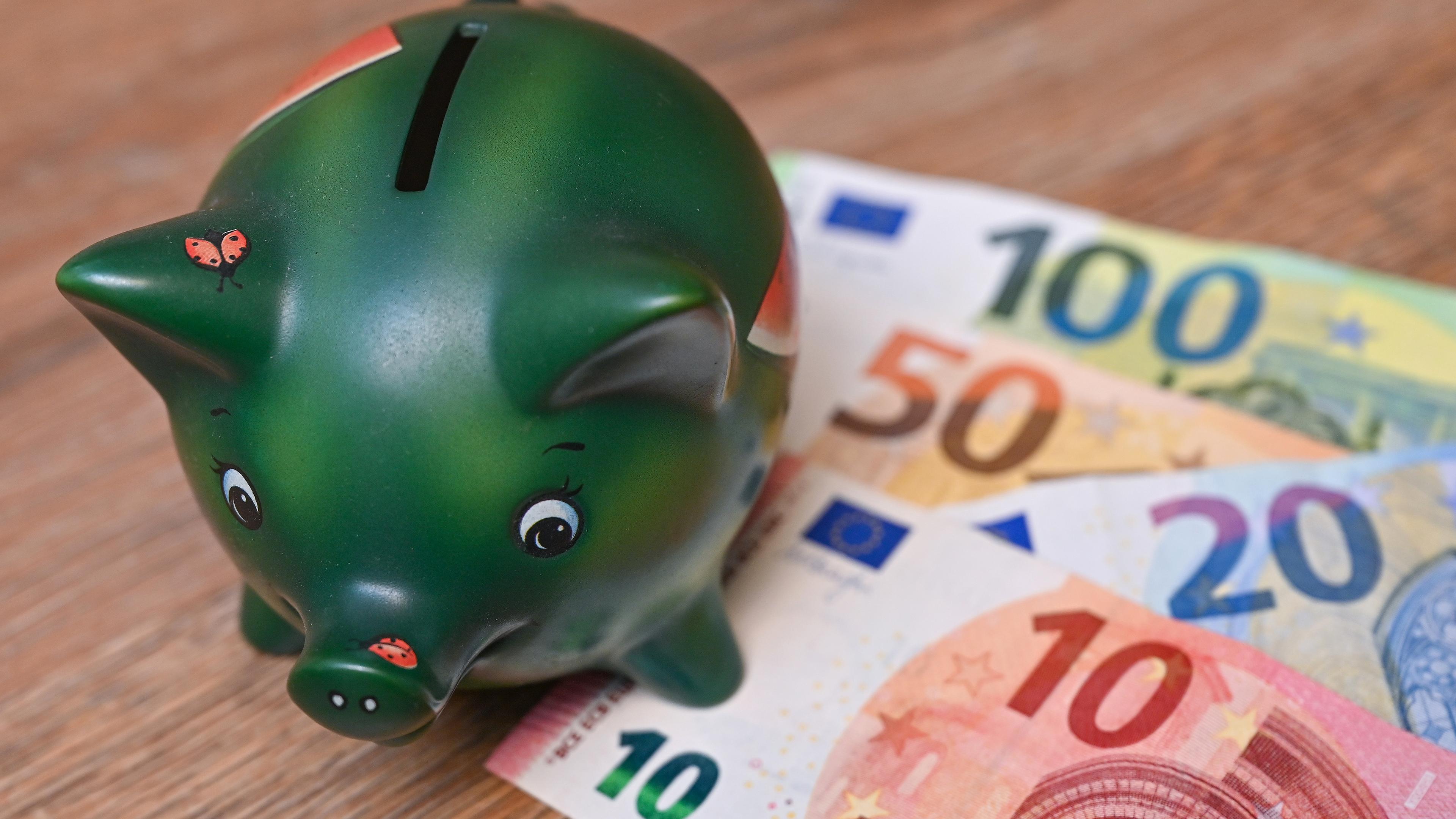 Ein Sparschwein steht auf einem Tisch neben Eurobanknoten (gestellte Aufnahme)