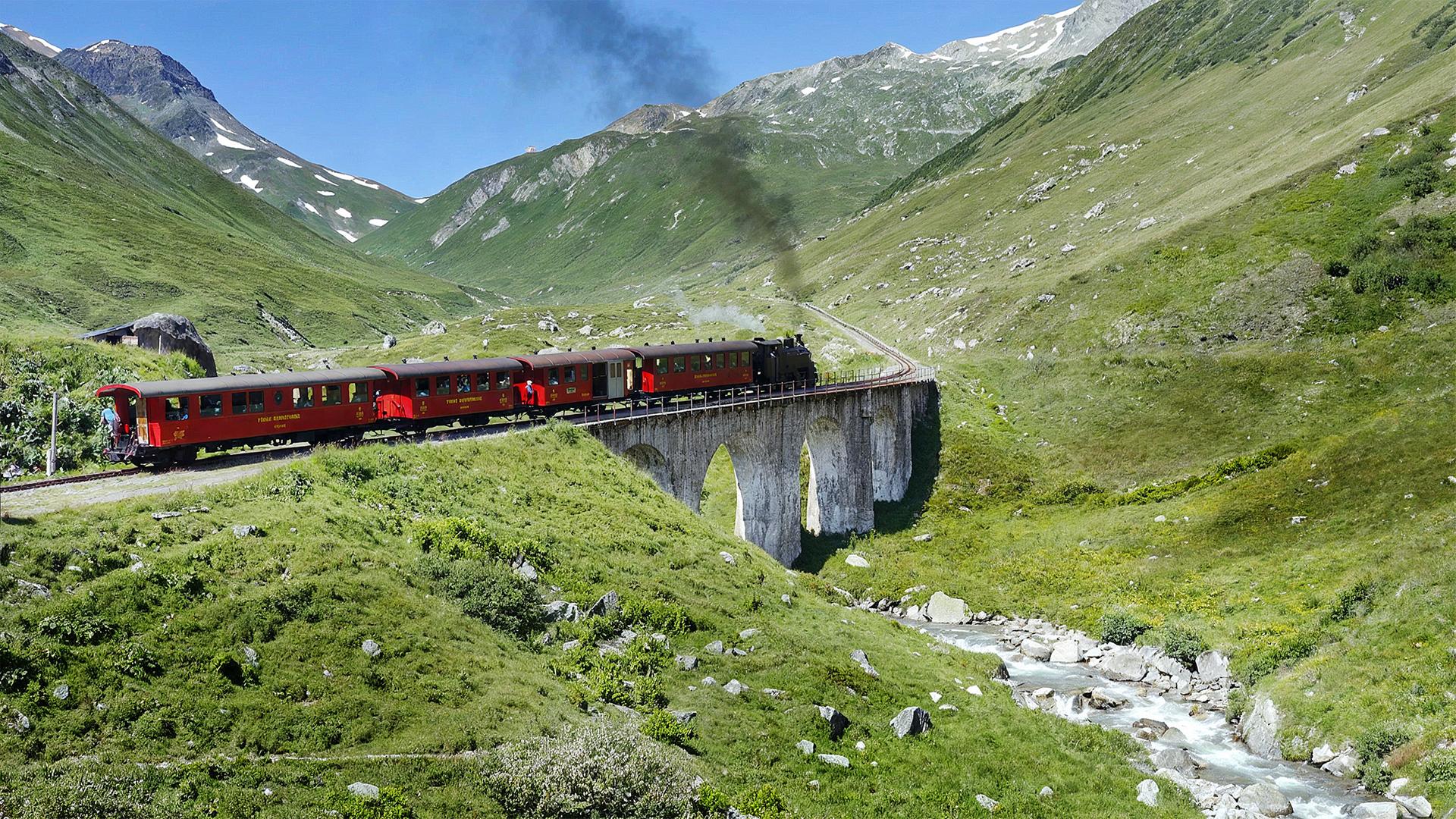 Zug fährt durch eine Berglandschaft über ein Aquaduct