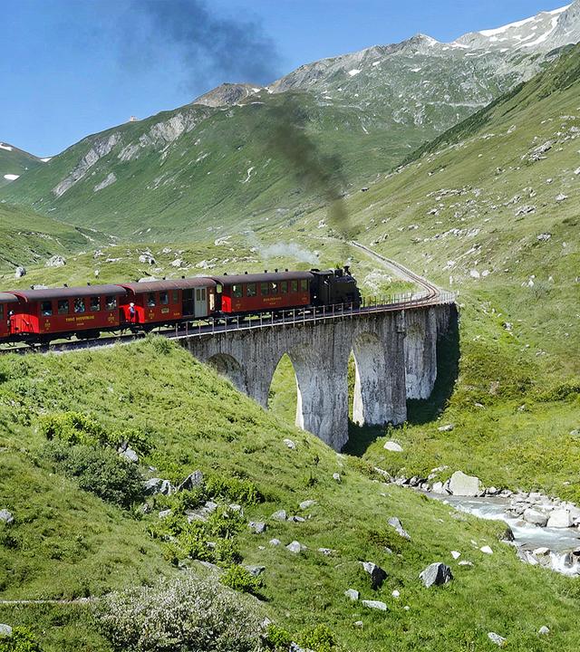 Zug fährt durch eine Berglandschaft über ein Aquaduct