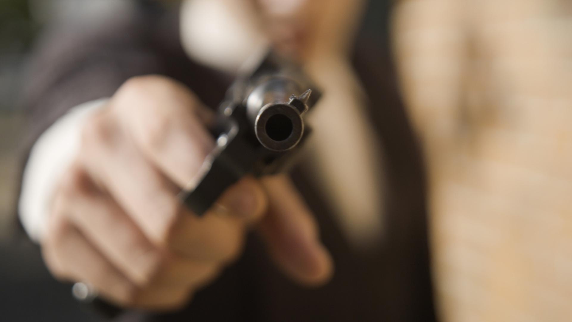Eine Person zielt mit einer Pistole direkt in die Kamera.
